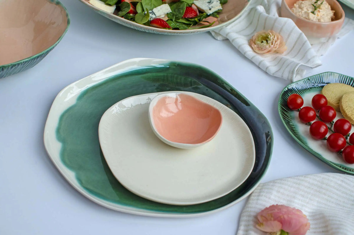 Green-rimmed porcelain plate with a pink bowl on a table set with salad and tomatoes