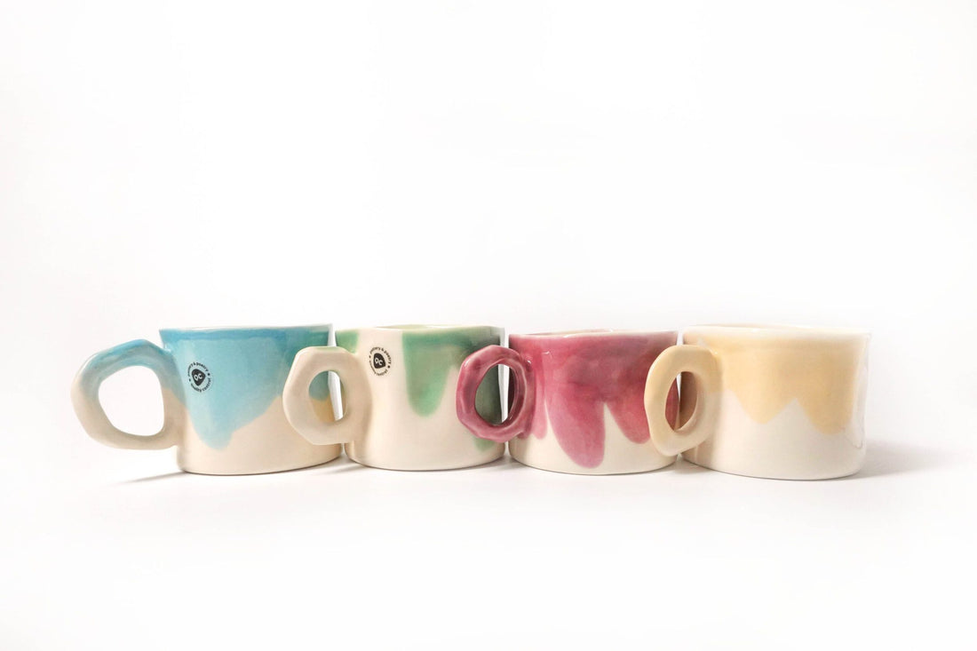 Handmade mugs with blue, green, pink and beige glazes arranged in a row
