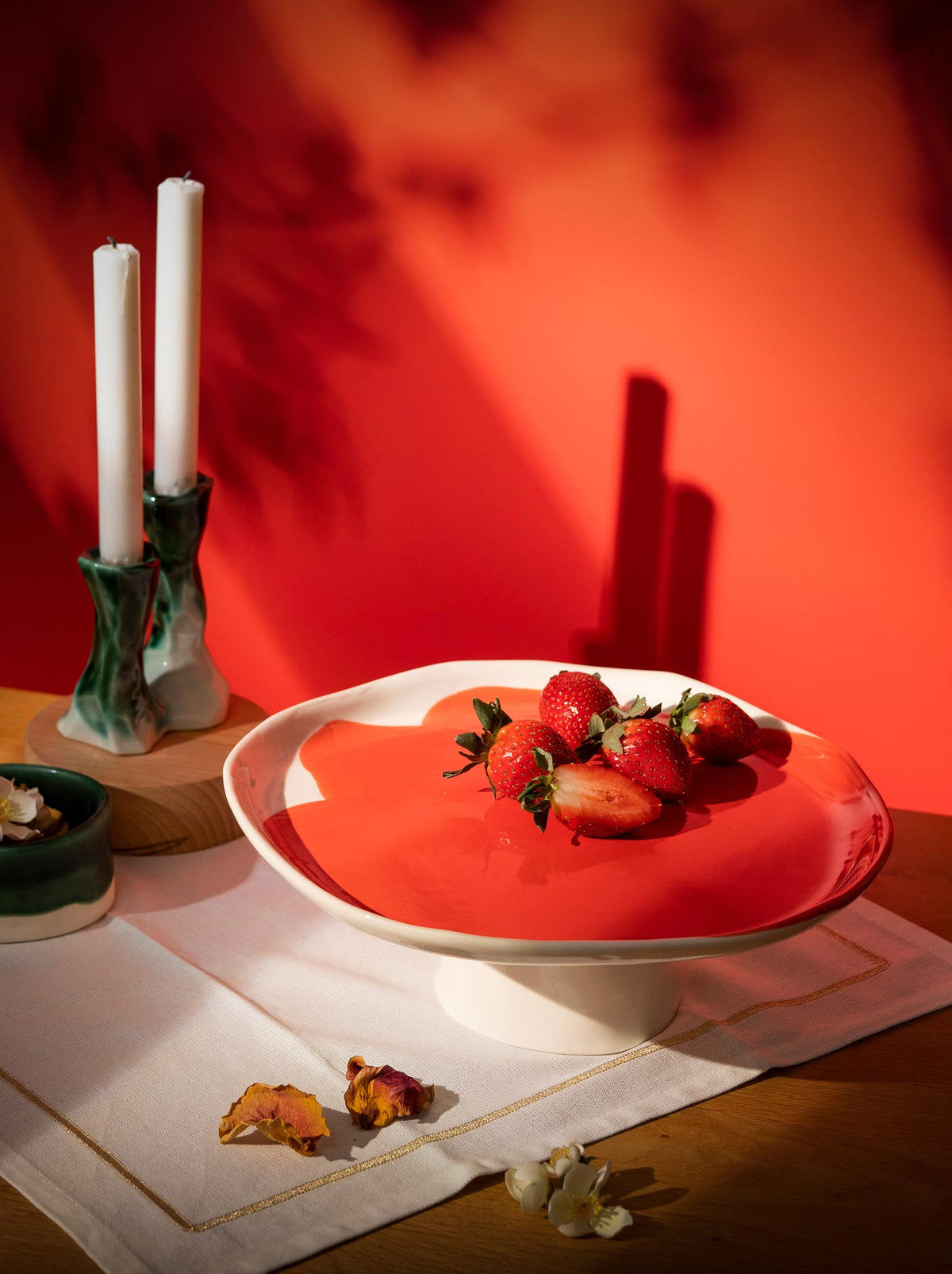 Red glazed ceramic cake stand with strawberries beside candles