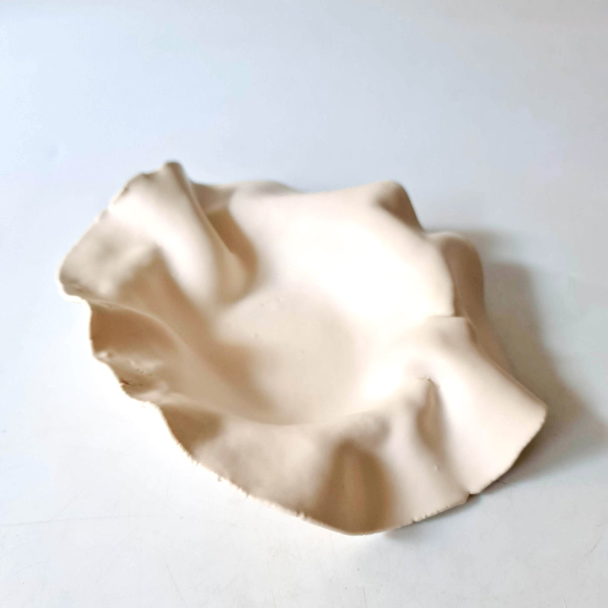 Ivory ceramic plate with a folded sculptural rim on a white background