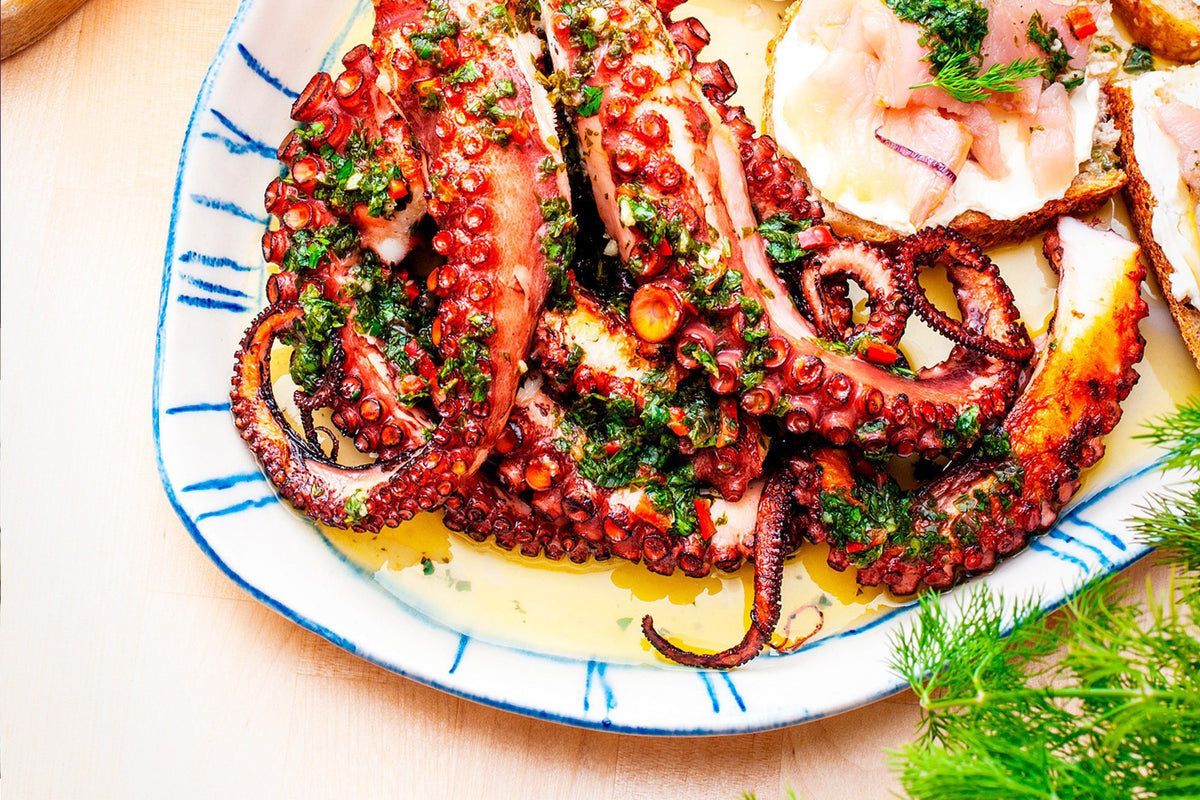 Grilled octopus served on a white fine dining plate with hand-painted blue lines