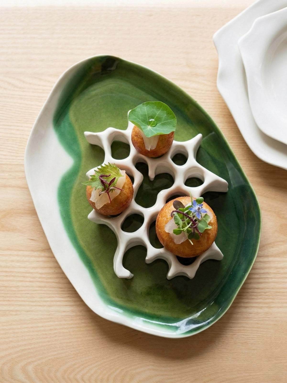 Chef's Table green glazed platter with a white porcelain honeycomb stand holding three garnished canapés