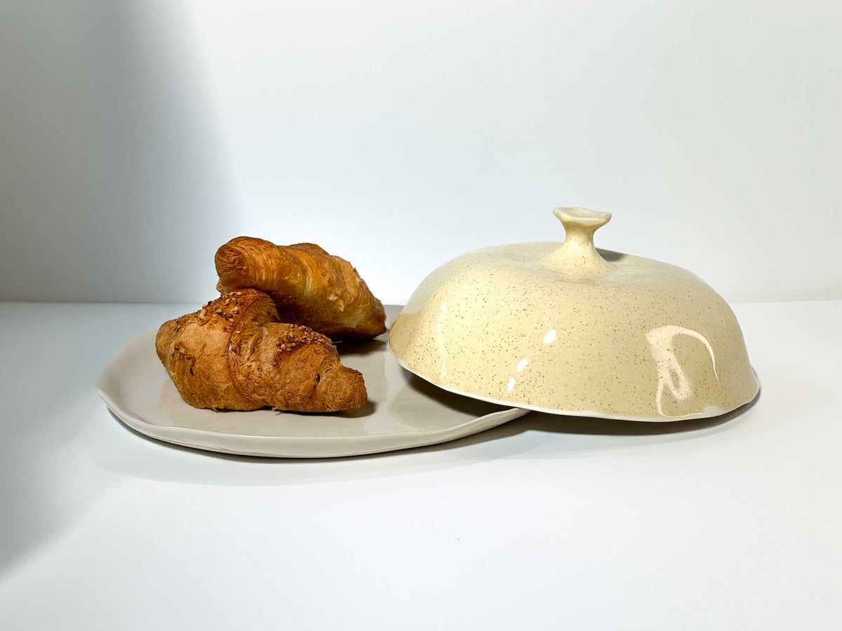 Ivory ceramic cheese box with a domed lid beside croissants