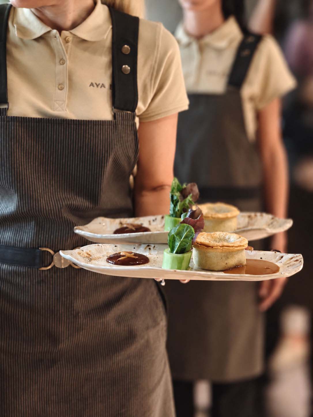Waiters at AYA Estate restaurant Salon carrying dishes on the handmade plates
