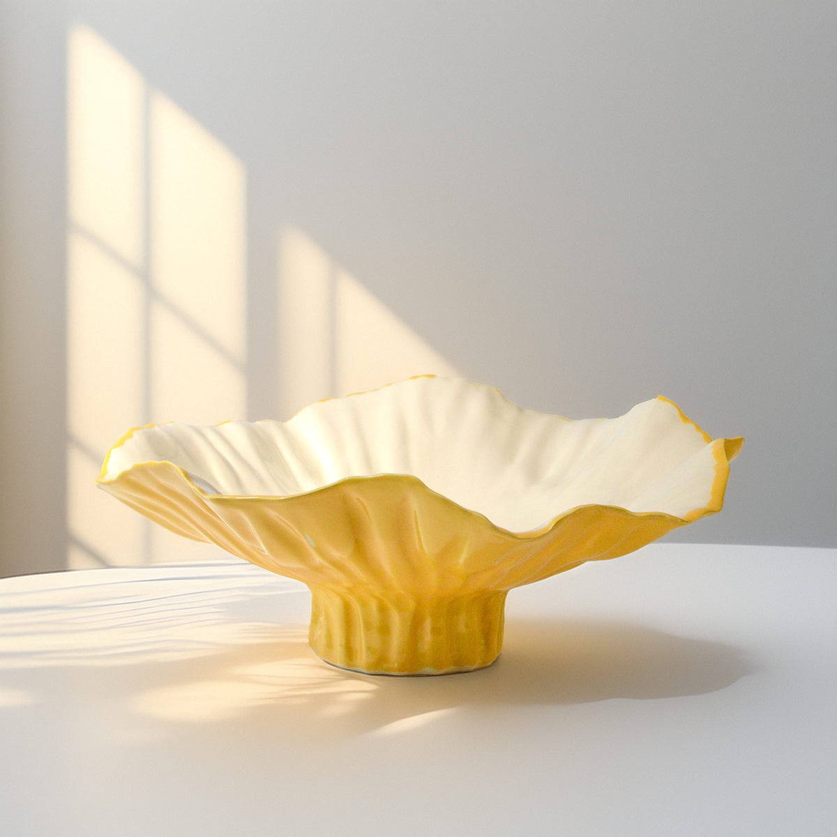 Yellow sculptural serving bowl with a flared ivory interior and a ribbed pedestal