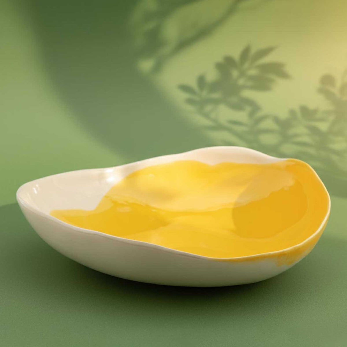 Yellow and ivory porcelain serving bowl on a green background with leaf shadows