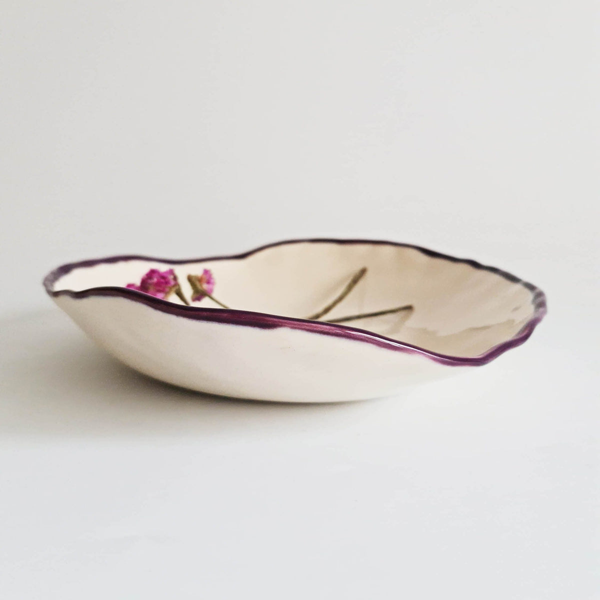Ivory oval serving bowl with a fine aubergine rim and a small floral accent