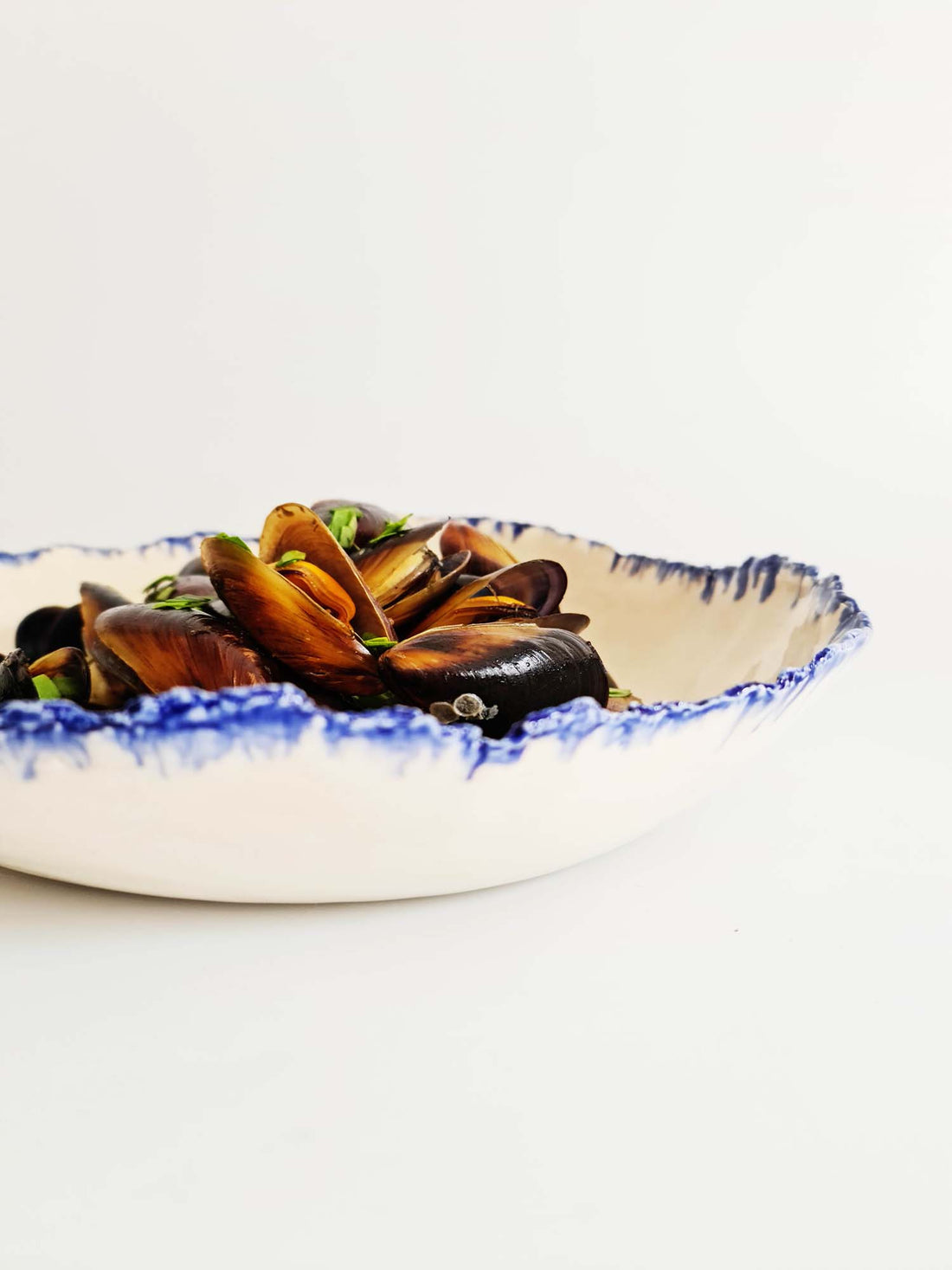 White handmade serving bowl with a running blue glaze rim, holding a cooked dish