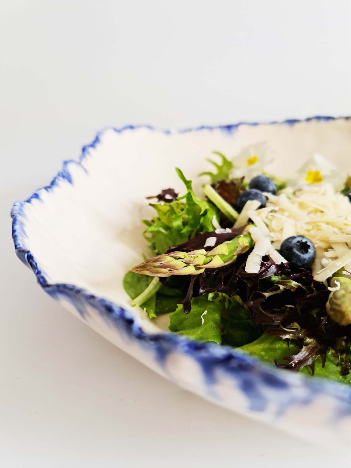 Close-up of a handmade bowl with a blue running glaze rim and salad inside