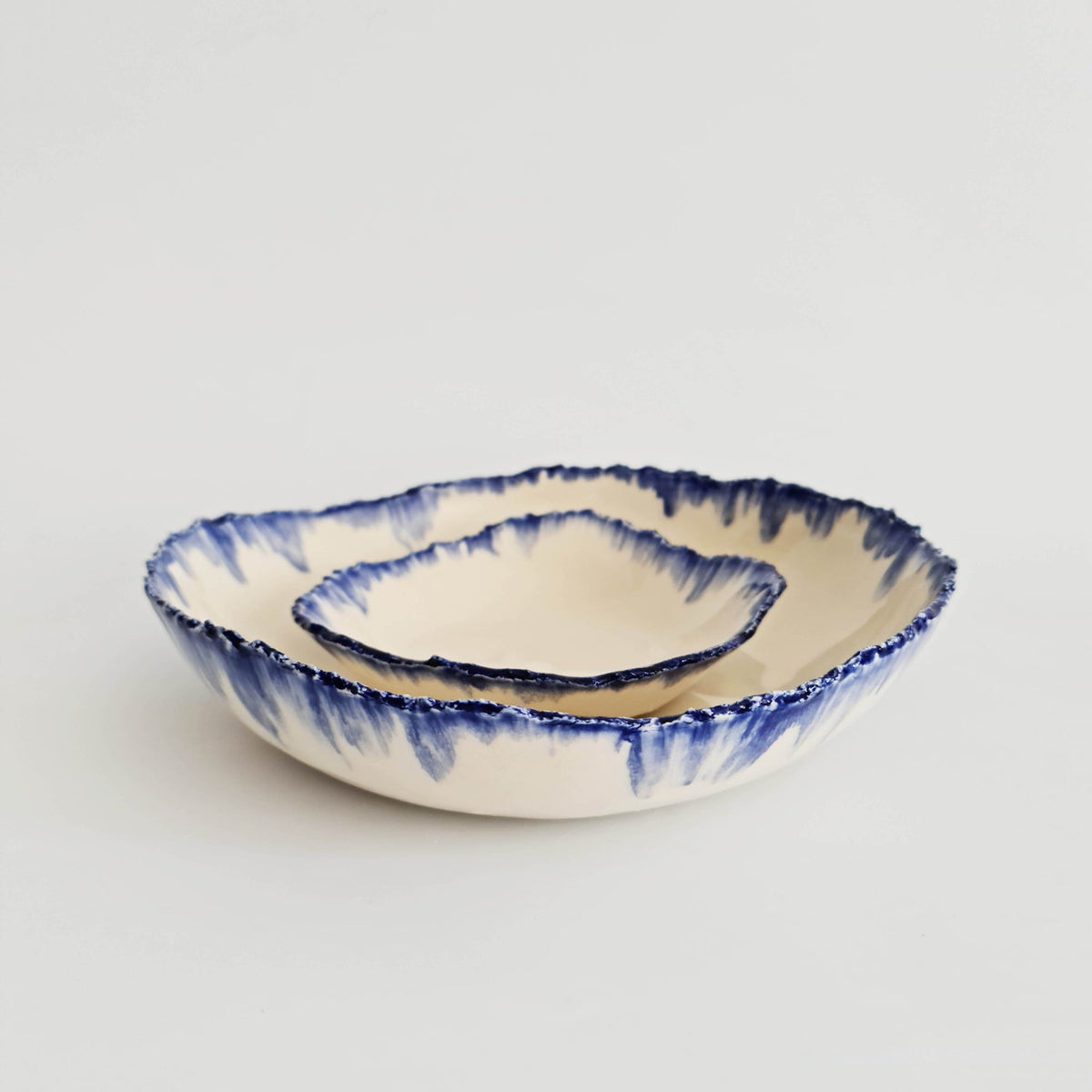 Two nested ivory ceramic serving bowls with irregular running blue glaze rims