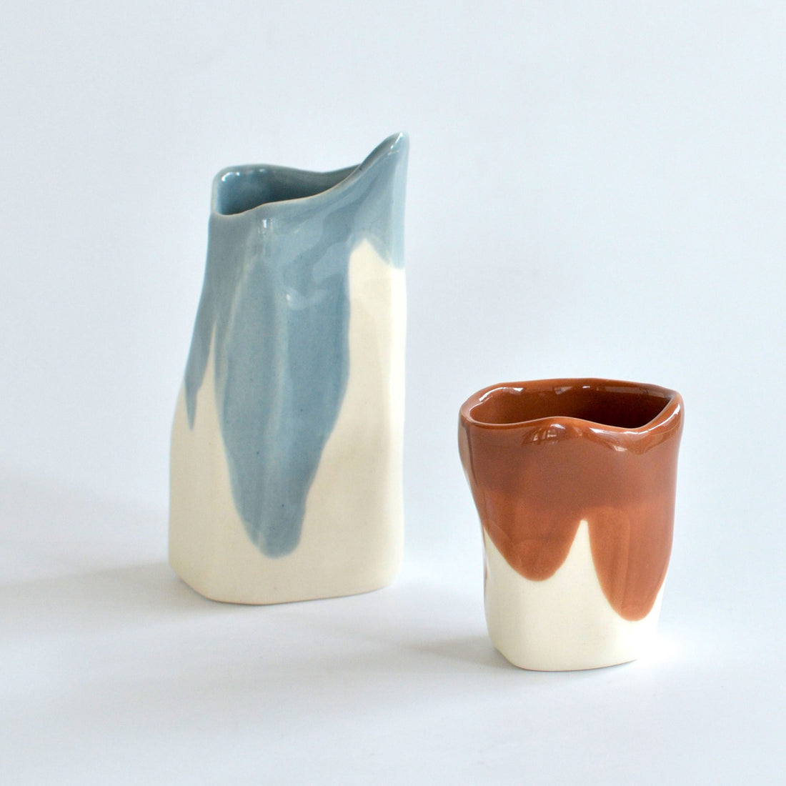 Handmade porcelain creamer in Light Denim glaze next to a terracotta coffee cup