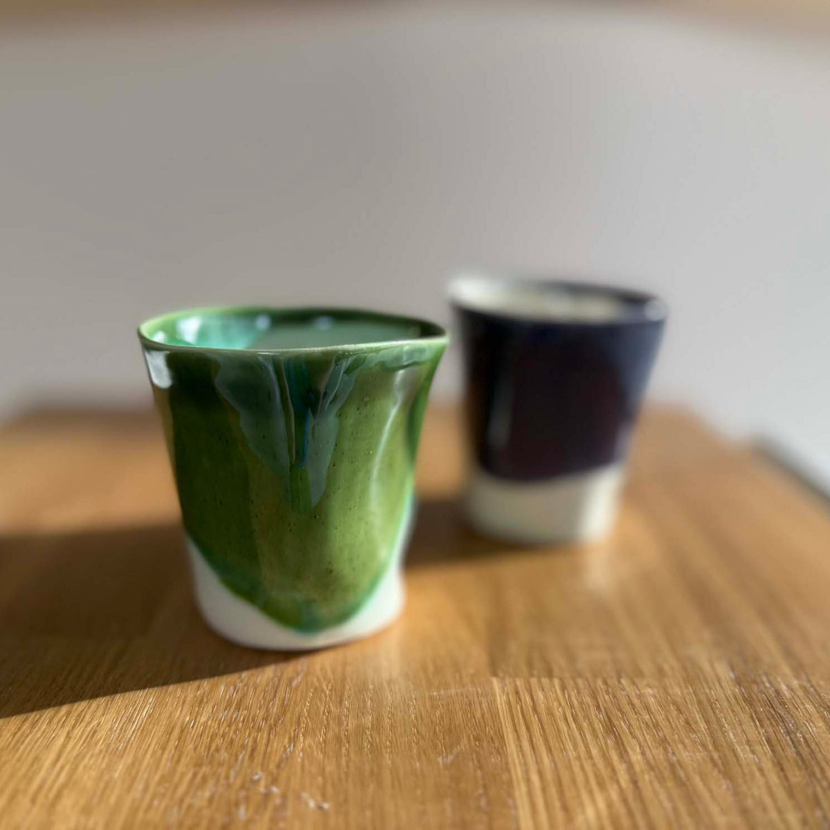 Green and dark blue handmade ceramic cups on a wooden table