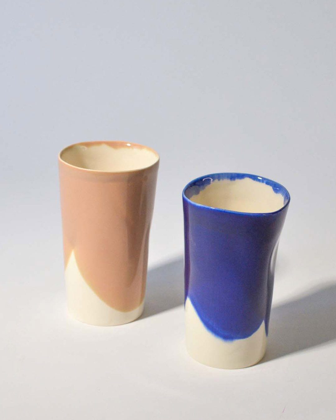 Peach and cobalt-blue tall ceramic cups shown upright on a white background