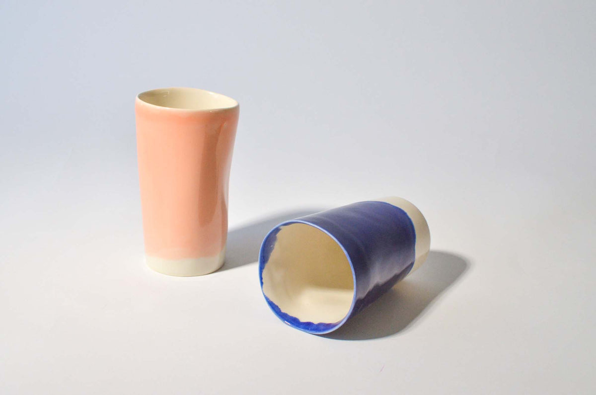 Tall peach ceramic cup beside a cobalt-blue cup lying on its side
