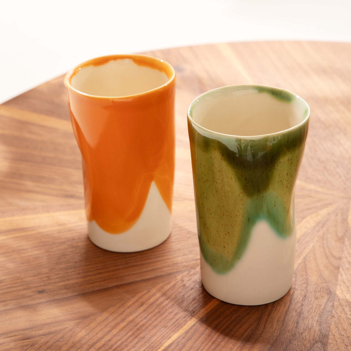 Orange and olive-green tall ceramic cups with exposed ivory bases on a wooden table