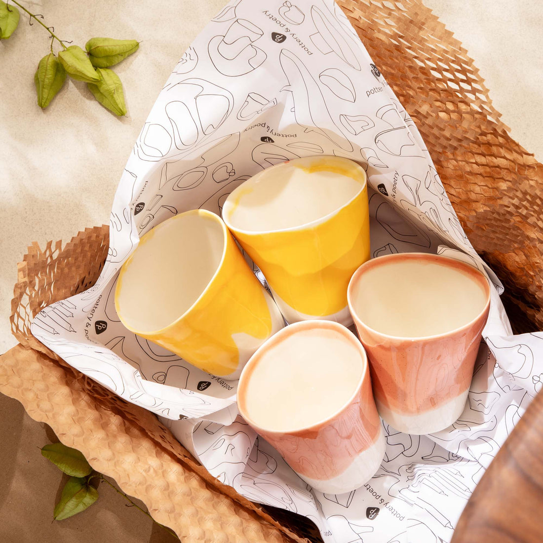 Four handmade ceramic cups in pale pink and yellow in a gift box