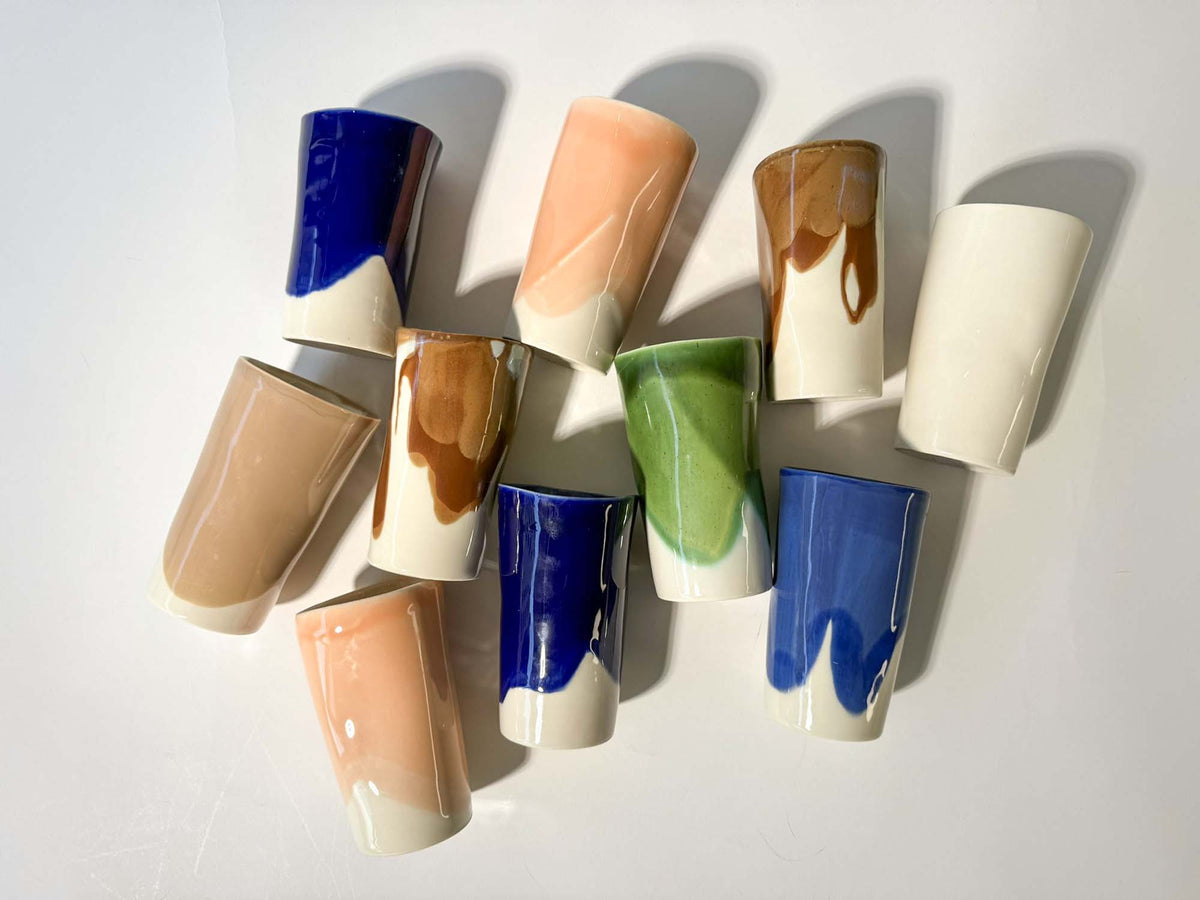 Tall handmade ceramic cups with blue, green, orange and pink glaze patches, arranged on white