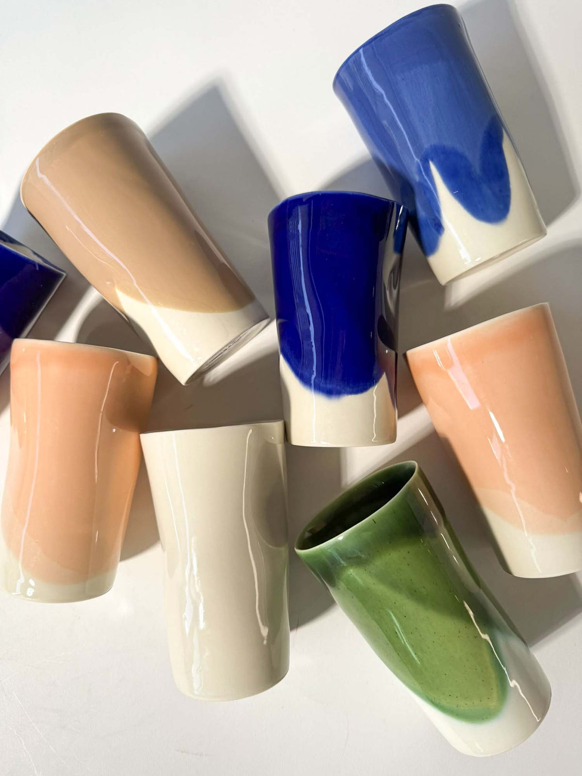 Close-up of tall ceramic cups with irregular blue, green and peach glaze boundaries