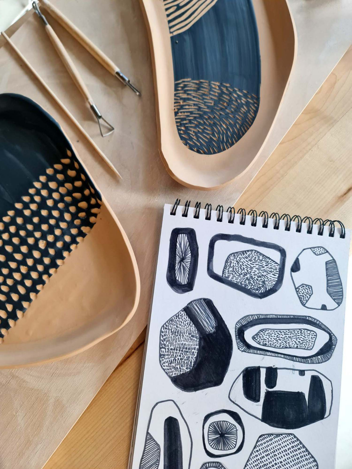 Sgraffito platters carved with blue patterns beside a sketchbook of designs and clay tools