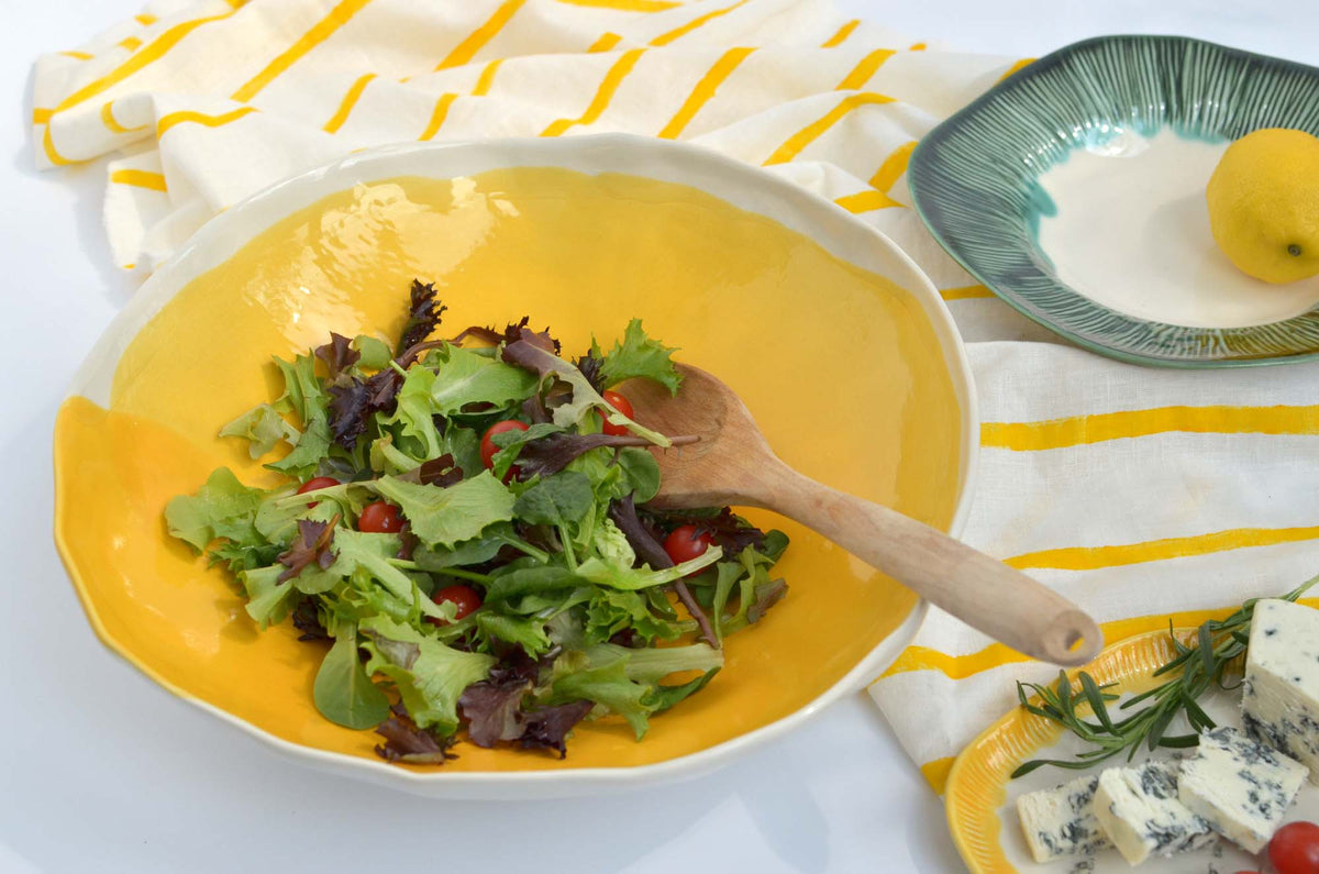 Food served on a yellow handmade ceramic plate beside green tableware