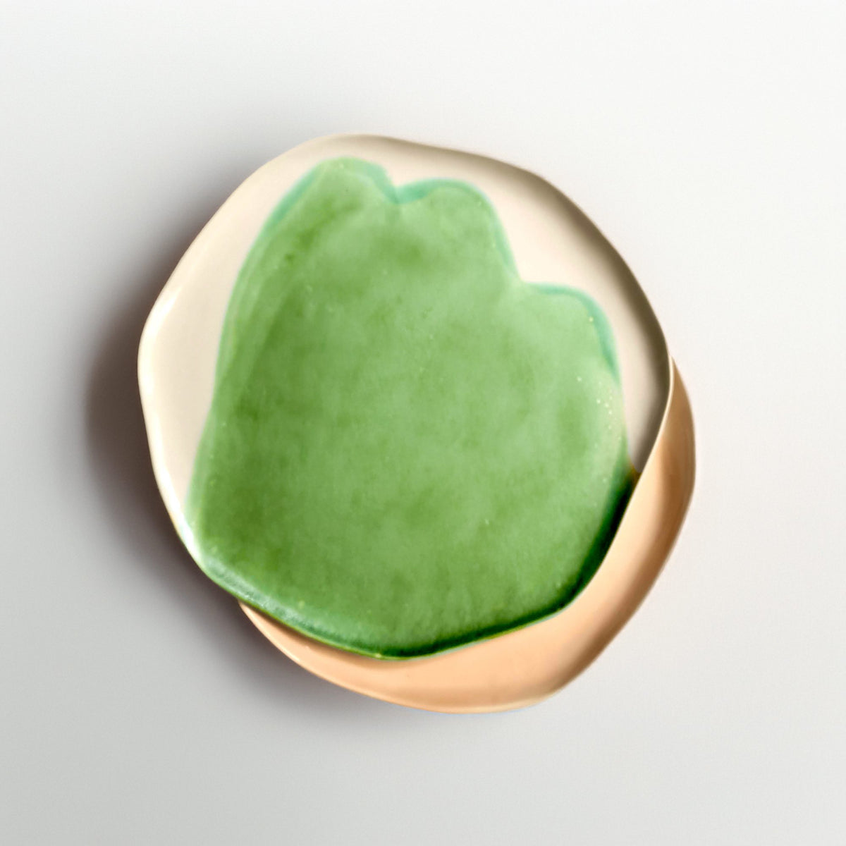 Green handmade ceramic side plate overlapping an ivory plate