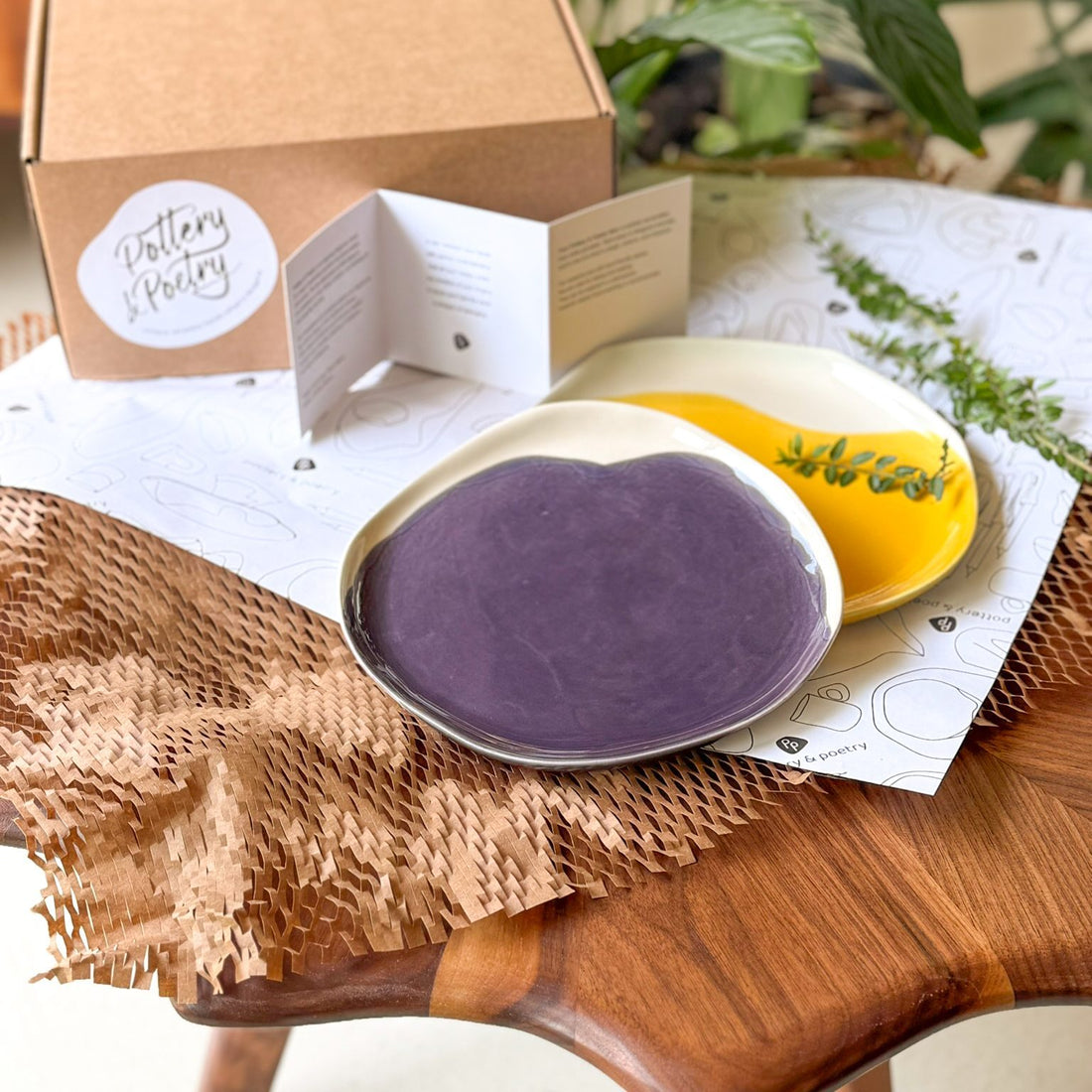 Purple and yellow handmade side plates beside a Pottery & Poetry gift box