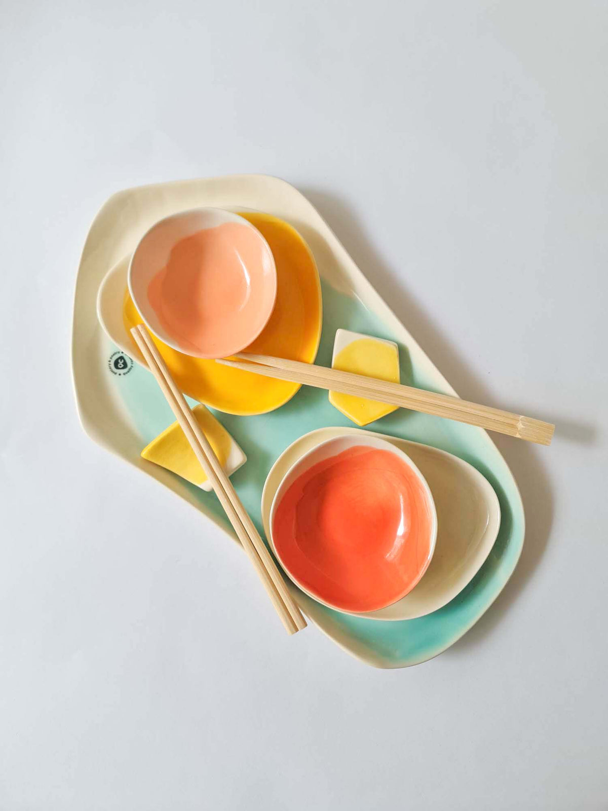 Stacked sushi set with turquoise and yellow trays, peach dip bowls and wooden chopsticks