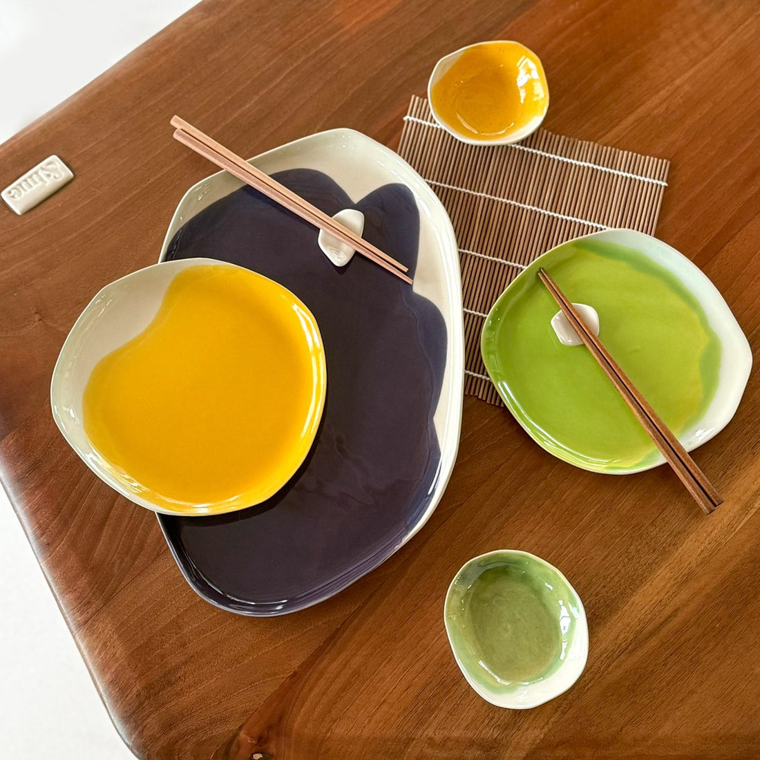 Sushi set for two on a wooden table: dark tray with yellow plate, green plate, dip bowls and chopsticks