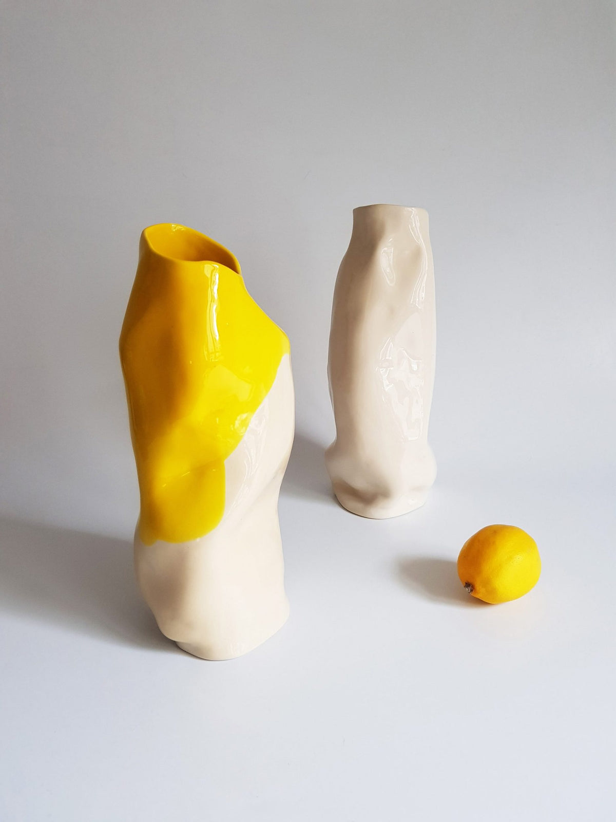 Tall handmade porcelain vases, one dipped in Lemon Yellow glaze, with a small lemon on a white table