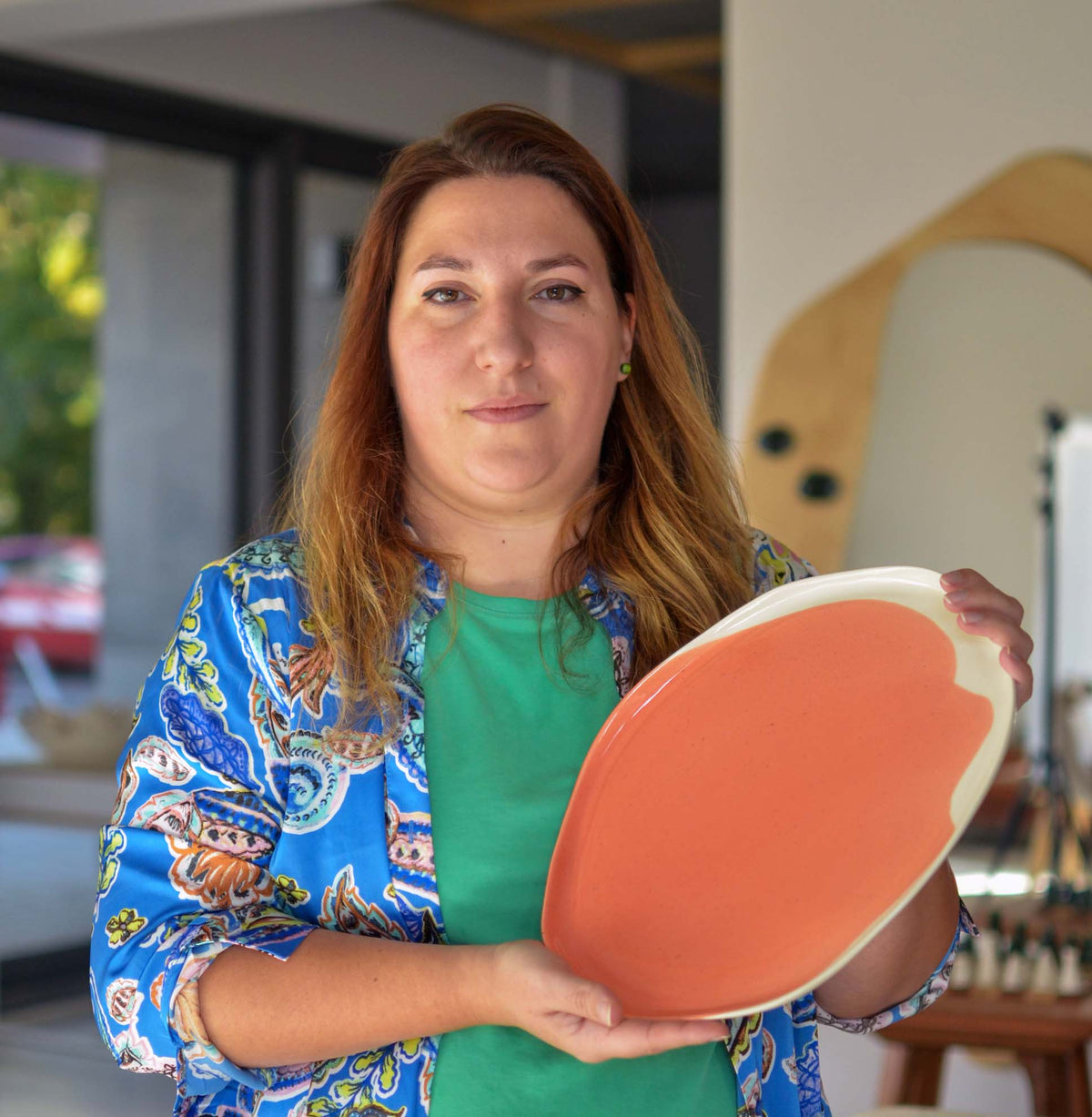 Mina Zlateva, ceramicist at Pottery & Poetry, holding a coral-glazed handmade porcelain plate