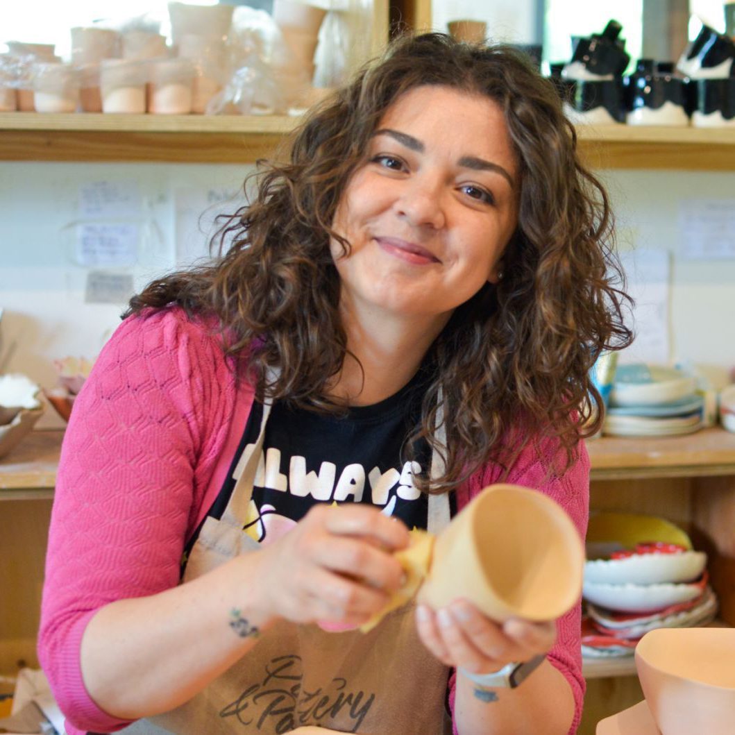 Irena Vakrilova, ceramicist at Pottery & Poetry, smoothing a porcelain cup in the studio
