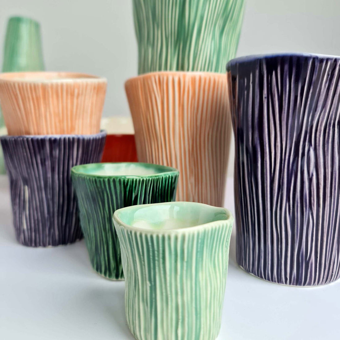 Handmade ceramic cups with vertical grooves in green, peach and purple glazes