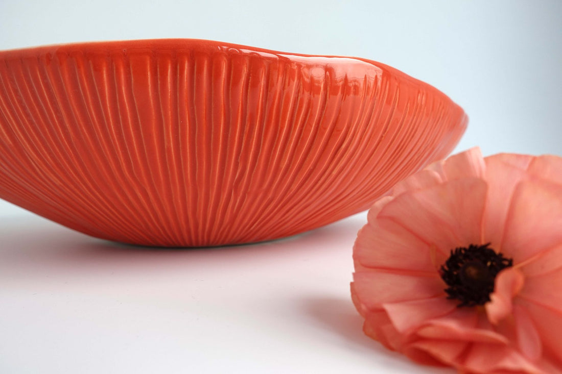 Textured large porcelain serving bowl in Ferrari Red glaze with ribbed exterior beside a pink poppy
