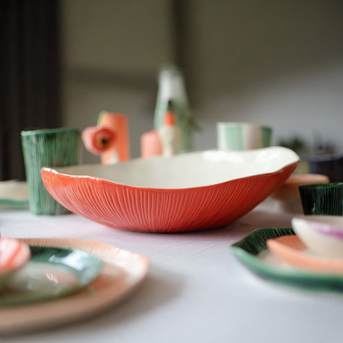 Large textured porcelain serving bowl in coral orange glaze with ribbed exterior on a set table