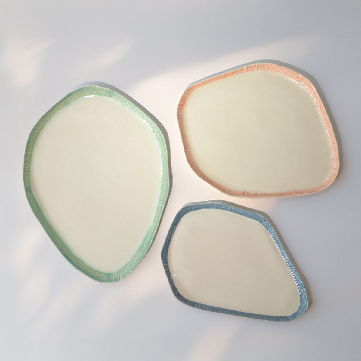 Three handmade porcelain trays with carved textured rims in mint, peach and blue