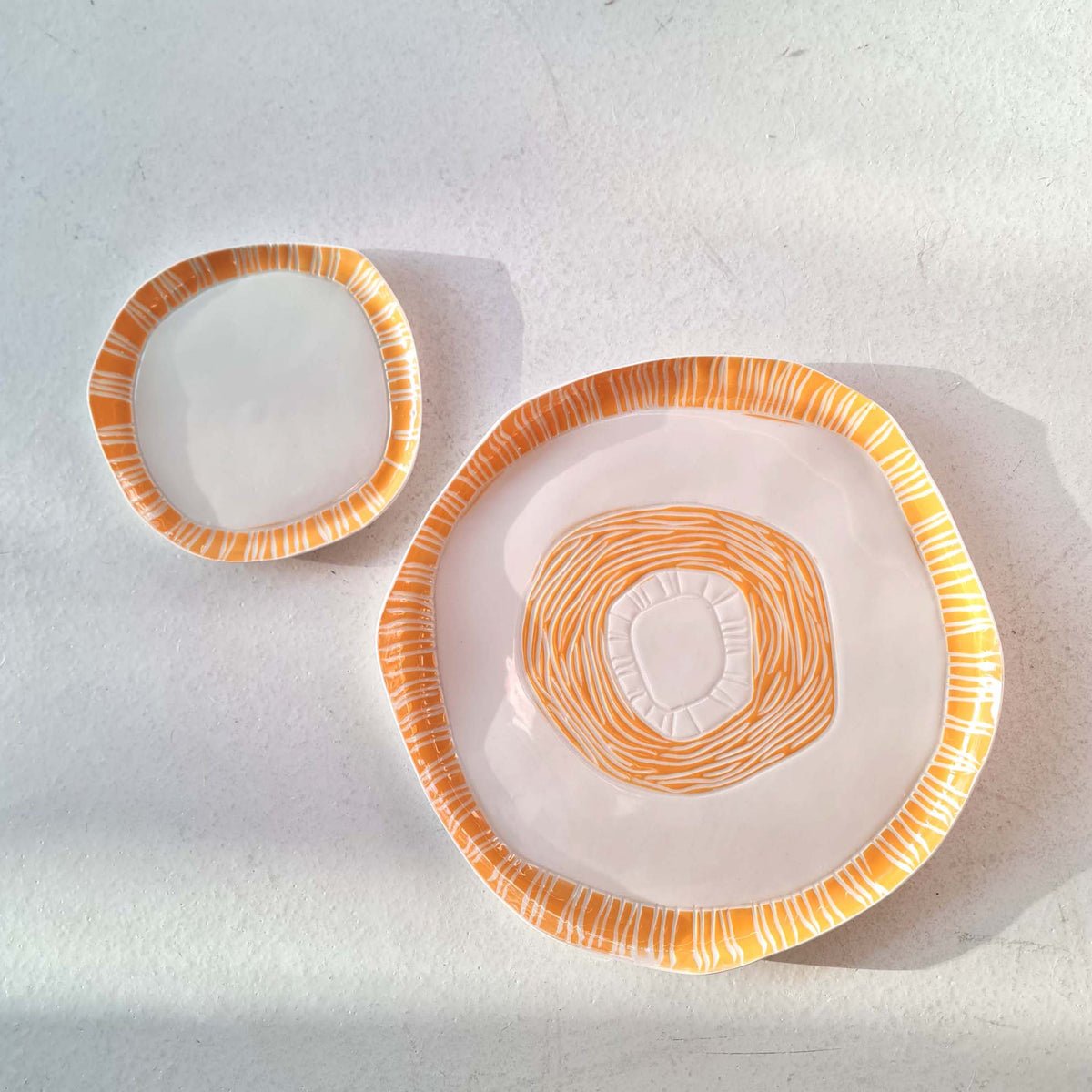 Two handmade porcelain plates decorated with orange sgraffito lines, from the Sgraffito collection