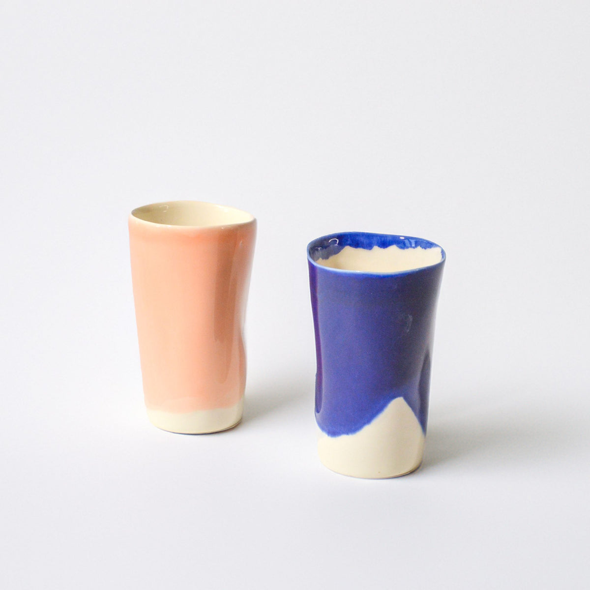 Two tall handmade cups with peach and cobalt-blue glazes on a white background