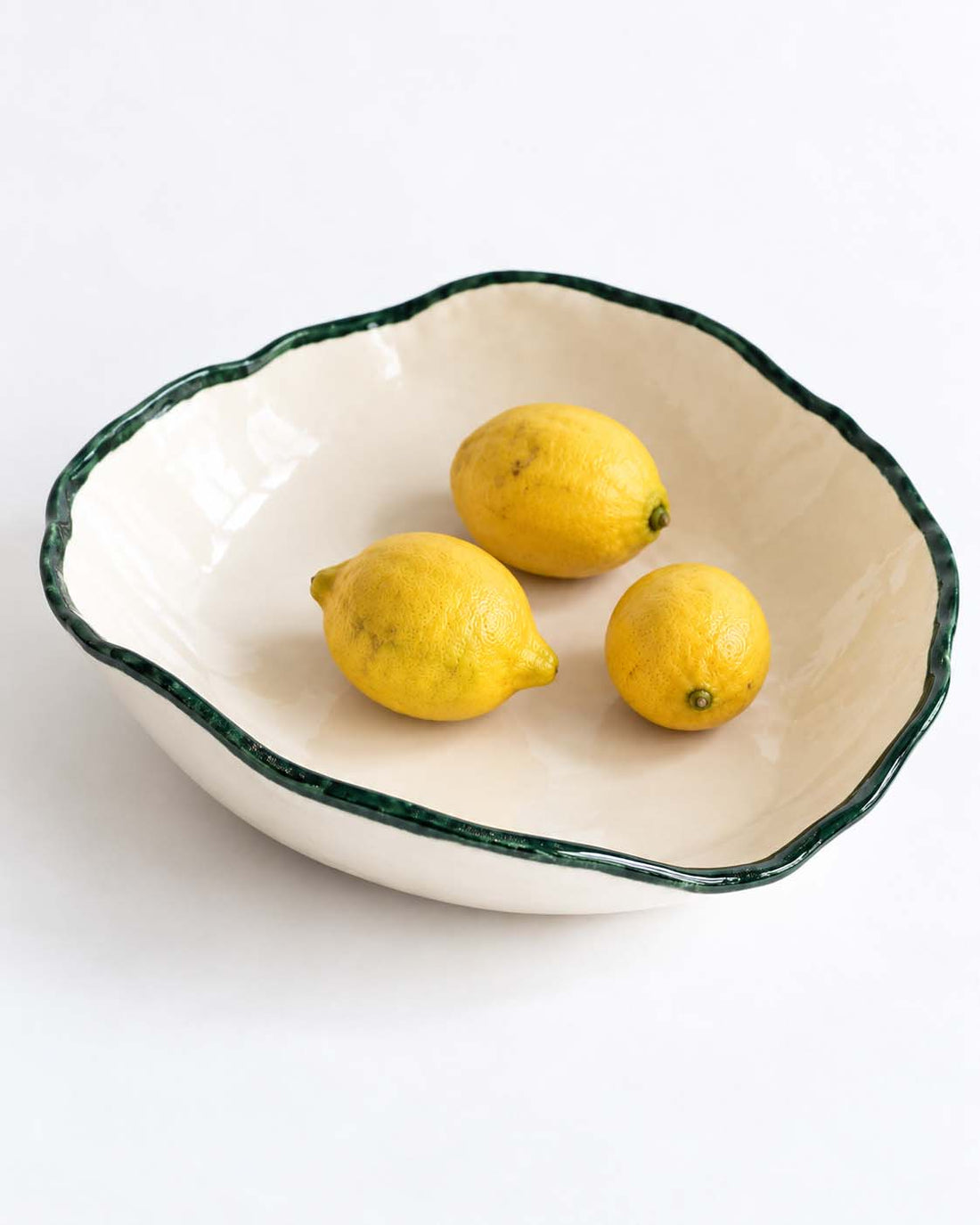 Ivory ceramic serving bowl with a glossy dark-green rim and three lemons