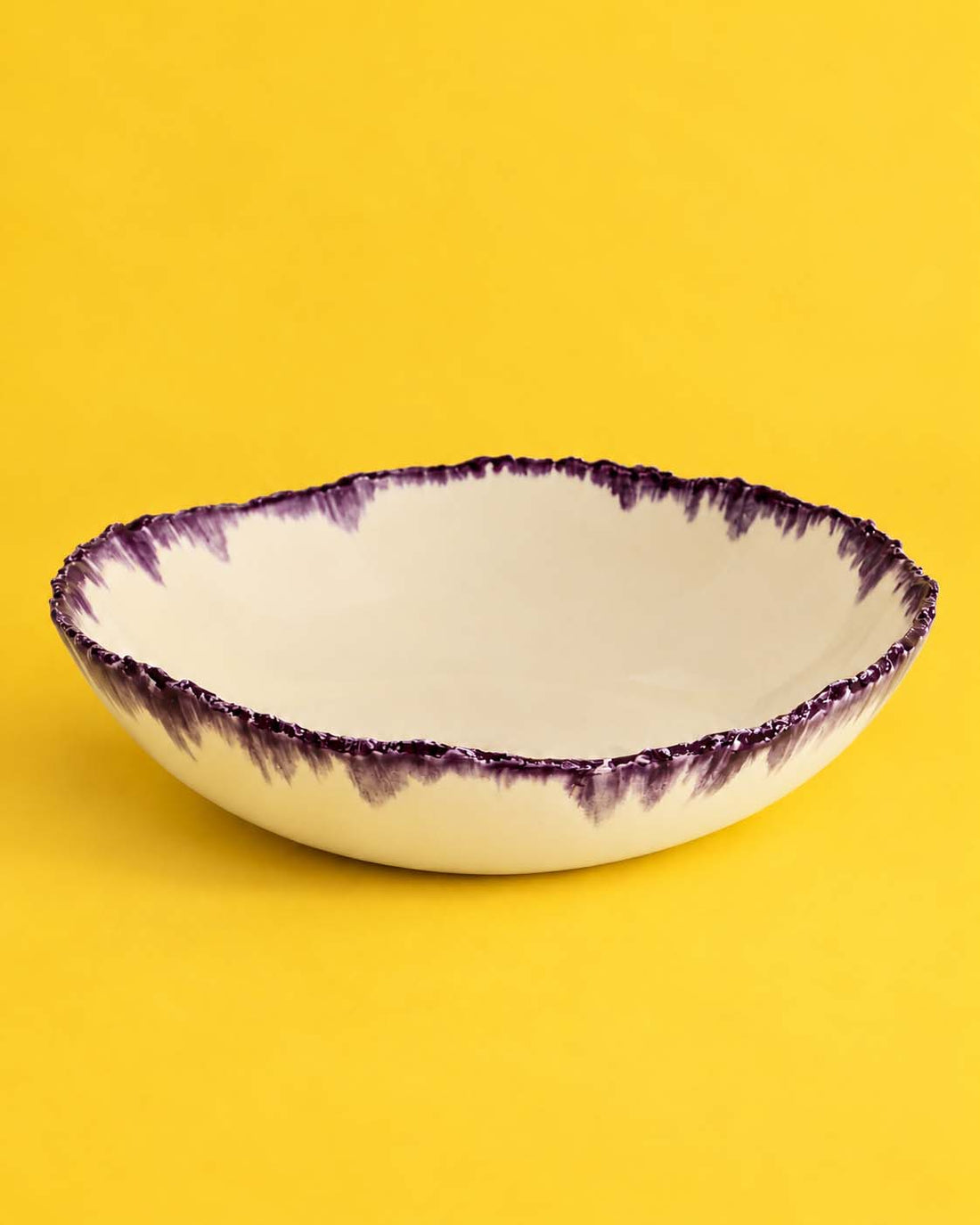 Ivory serving bowl with an irregular aubergine glaze rim on a yellow background