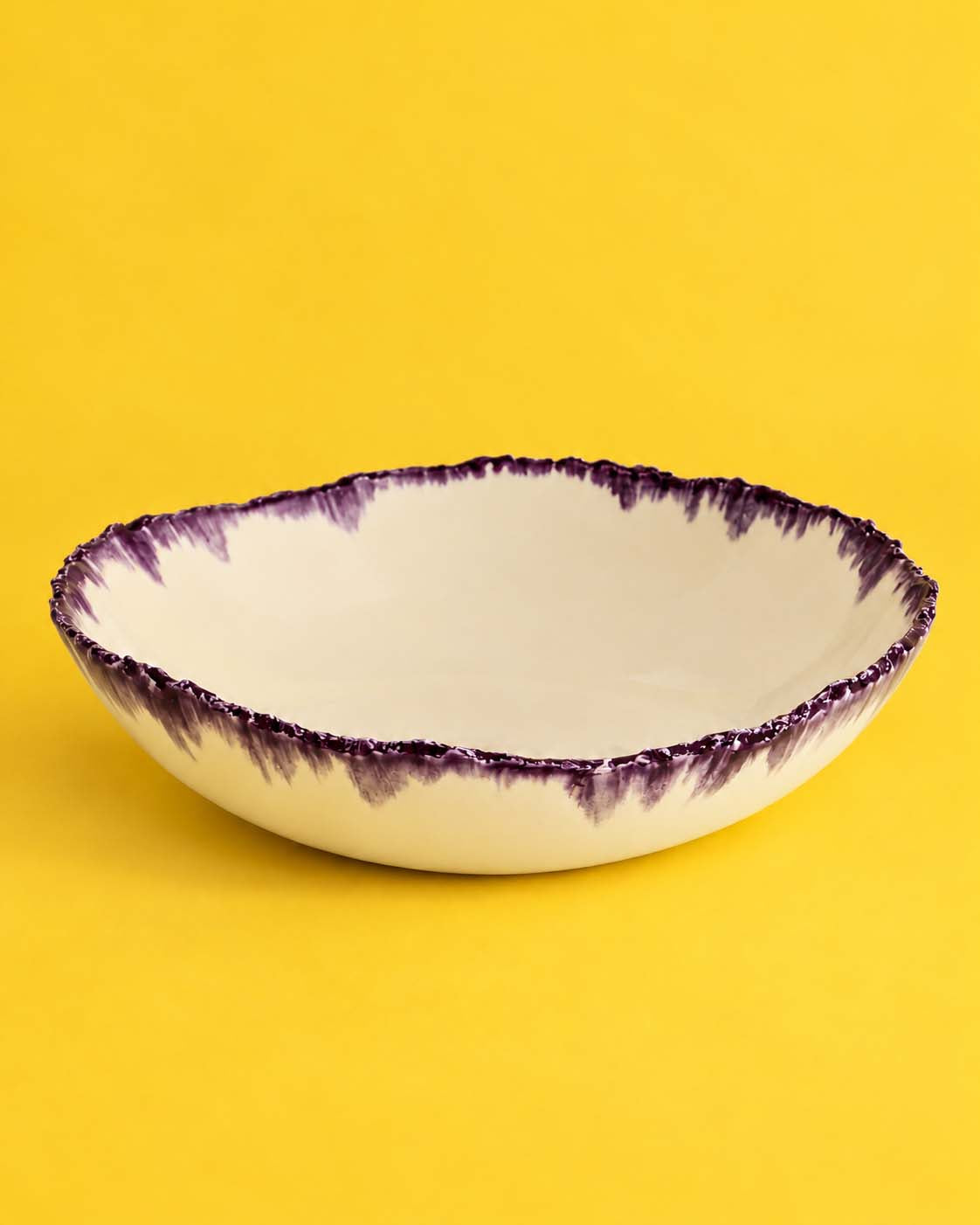 Ivory serving bowl with an irregular aubergine glaze rim on a yellow background