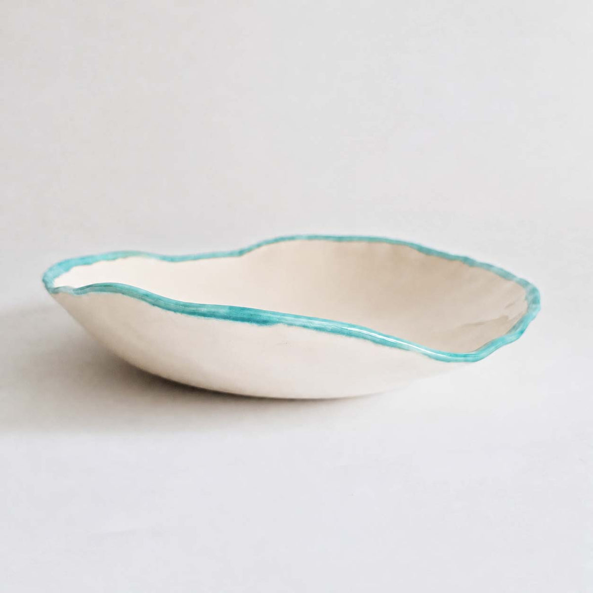 Ivory oval serving bowl with a light turquoise rim on a white background