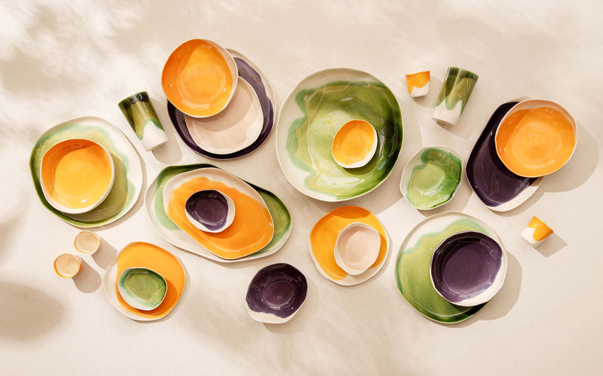 Handmade ceramic dinnerware in autumn glazes of saffron, sage green and aubergine laid on cream linen