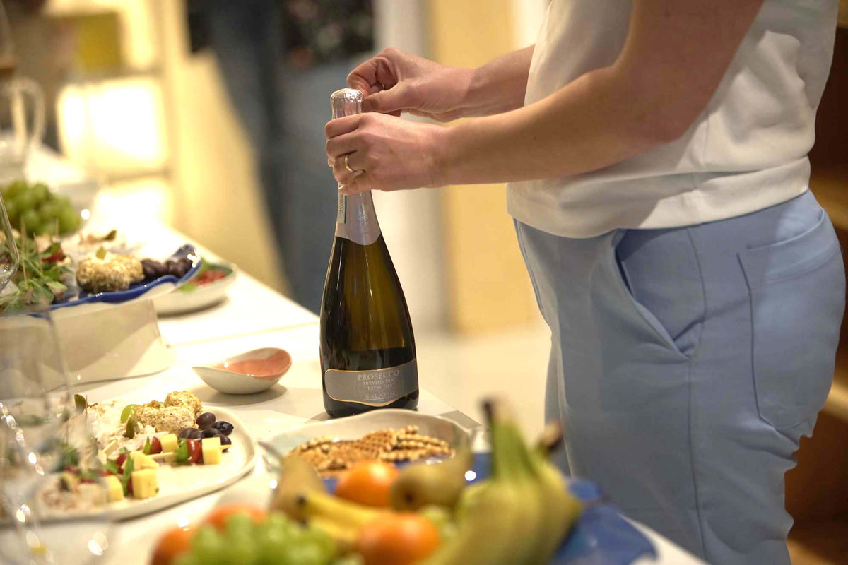 Guest opening sparkling wine beside a buffet of fruit and snacks at a private ceramics workshop