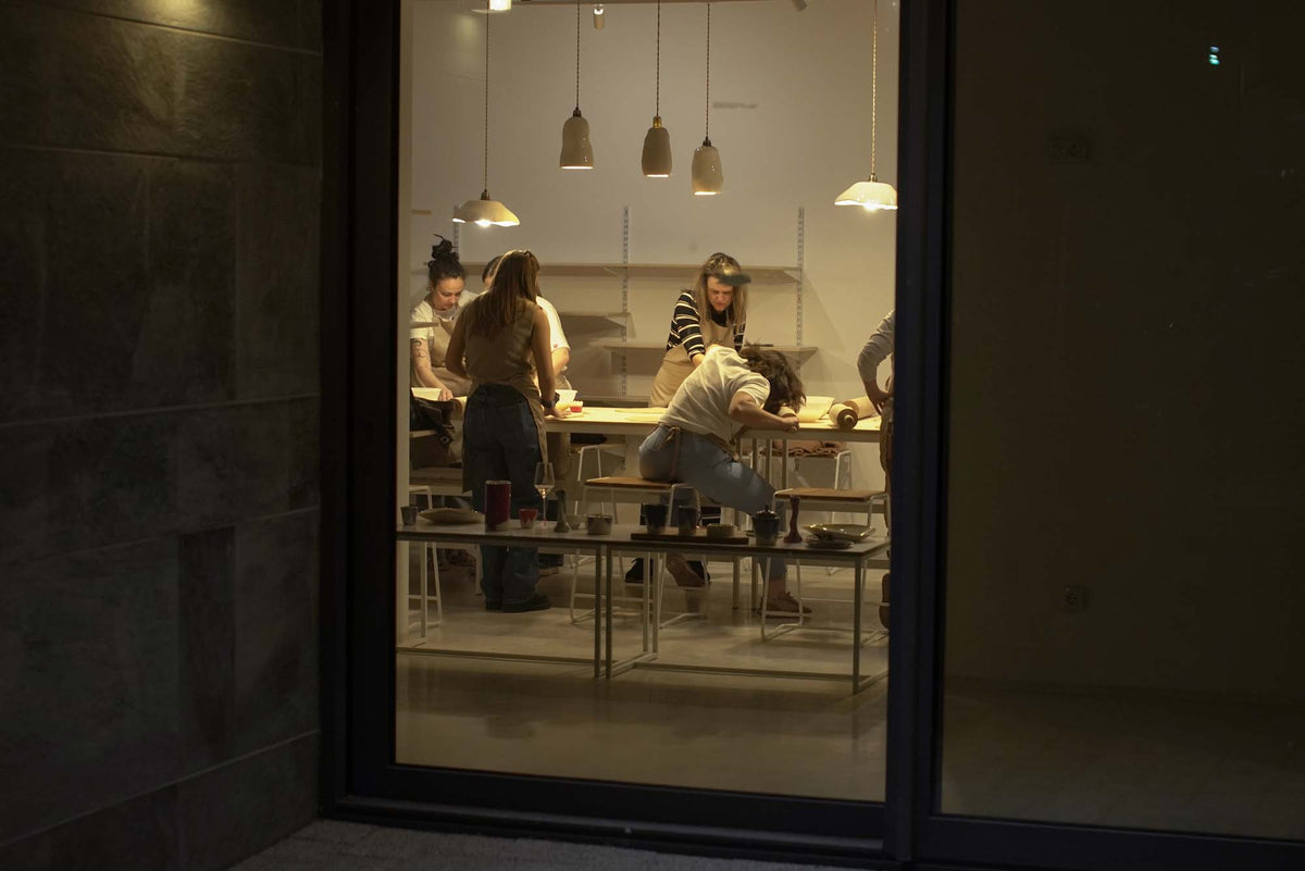 Evening view through glass doors into the studio as a group works at a ceramic workshop