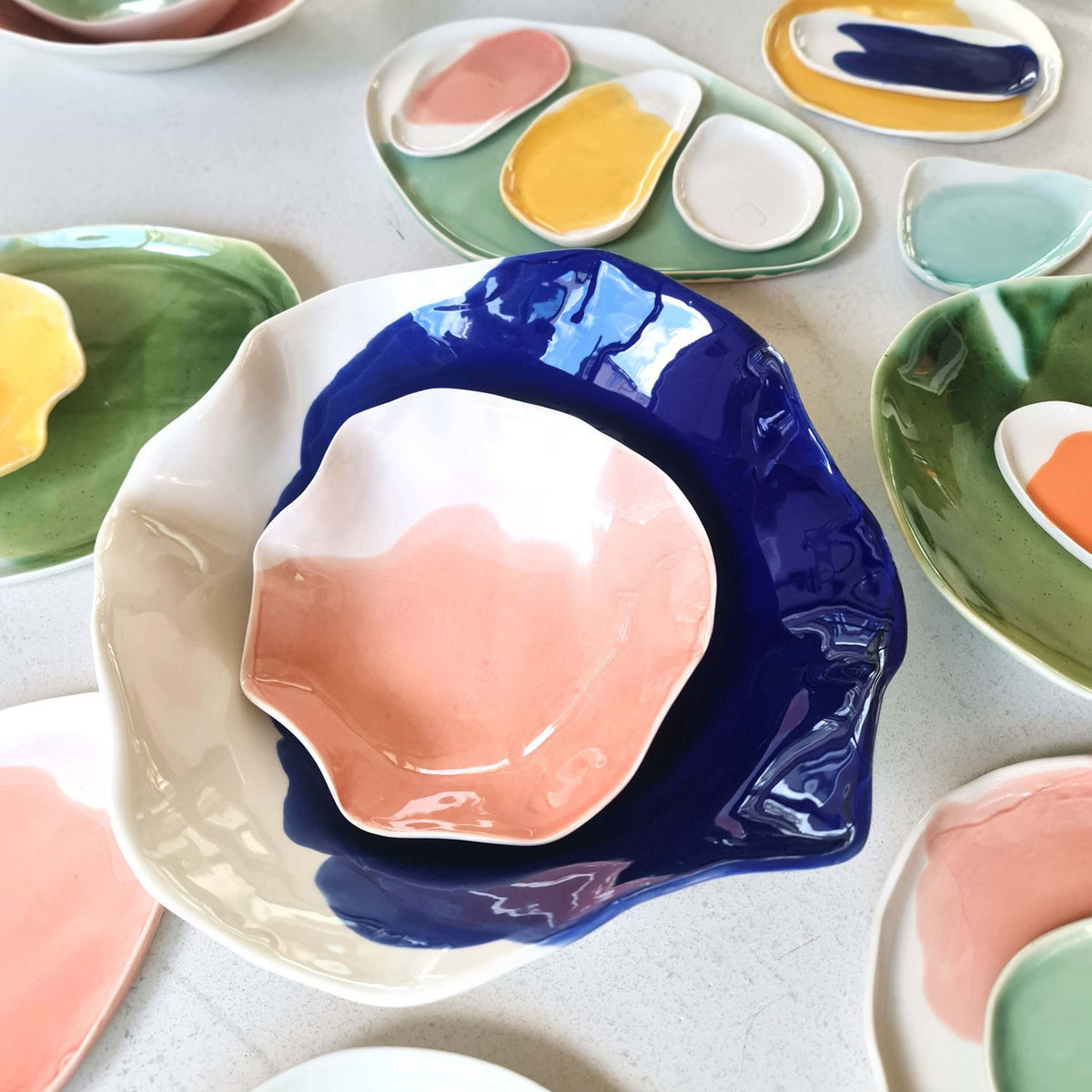Wavy handmade porcelain bowls in pink, royal blue and green glazes made by workshop guests