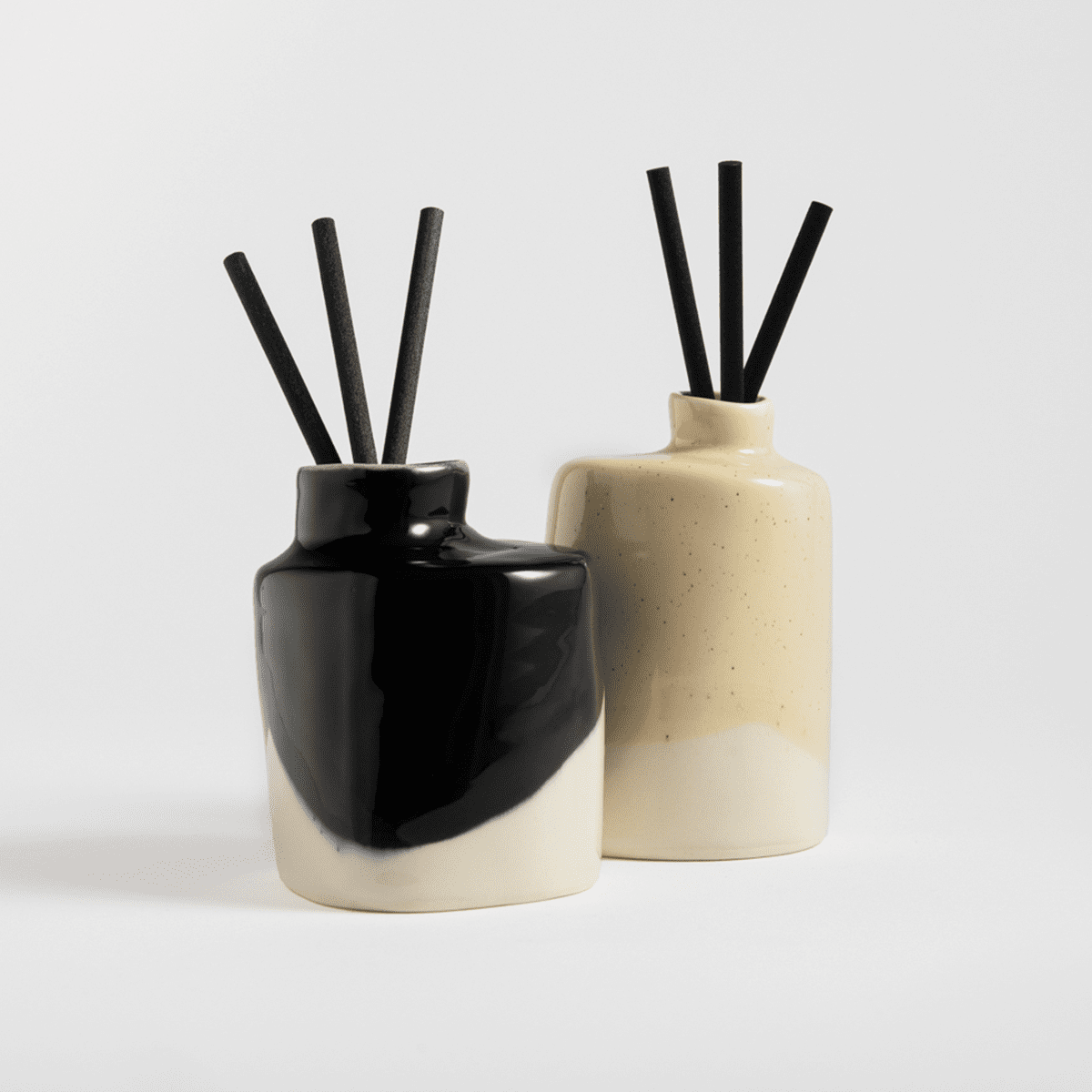 Two handmade porcelain scent diffusers in black and cream colors with black reeds.