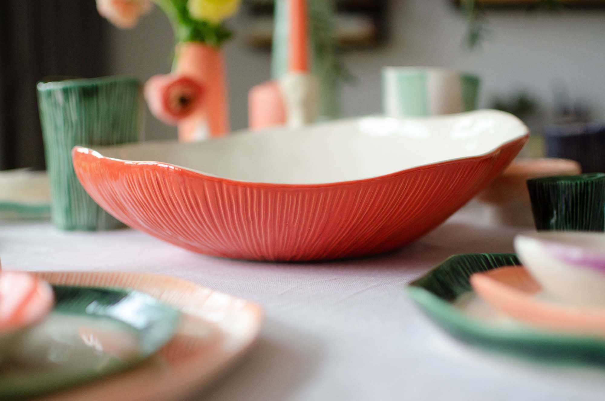 Ferrari Red textured bowl (2) Close-up of a large handmade porcelain bowl with red textured exterior and white interior, surrounded by matching colorful ceramic tableware.