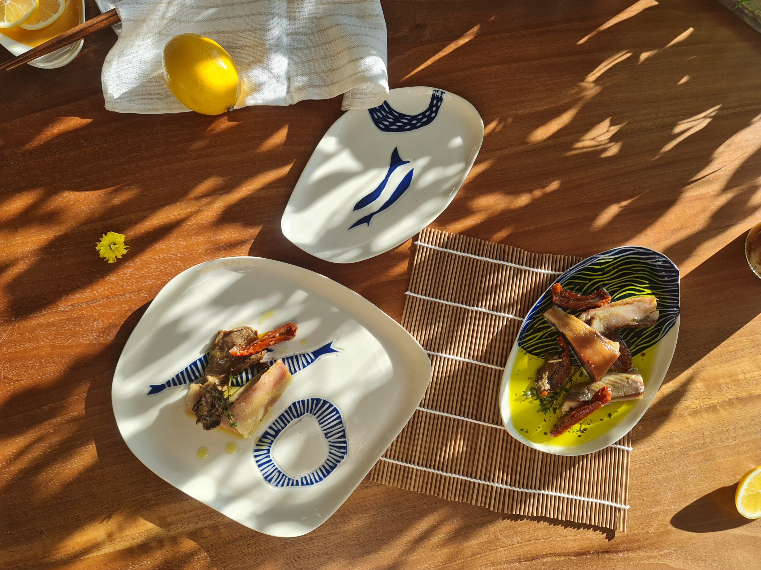 black sea catch collab (64) Porcelain fish plates with blue sgraffito designs, served with seafood dishes on a sunlit wooden table.