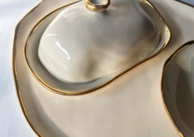 Close-up of a sculptural porcelain butter dish with organic contours and gold luster edging