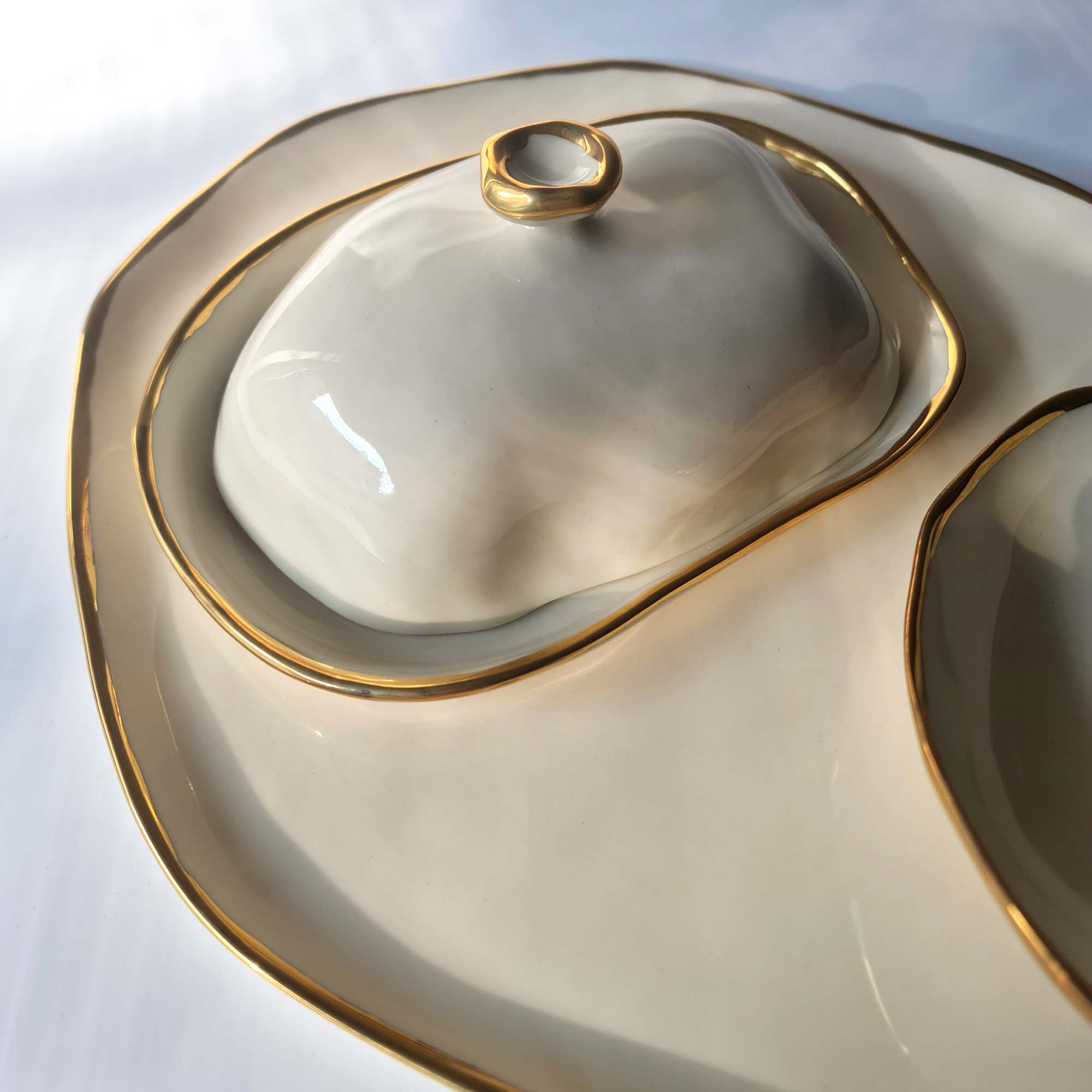 Close-up of a sculptural porcelain butter dish with organic contours and gold luster edging